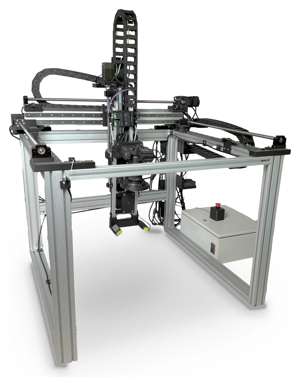 The OpenDerm prototype: a 3-axis aluminum-extrusion gantry with a DSLR camera on a pan-tilt head at its center, overhead cable chains, and a white electrical cabinet with an emergency stop.