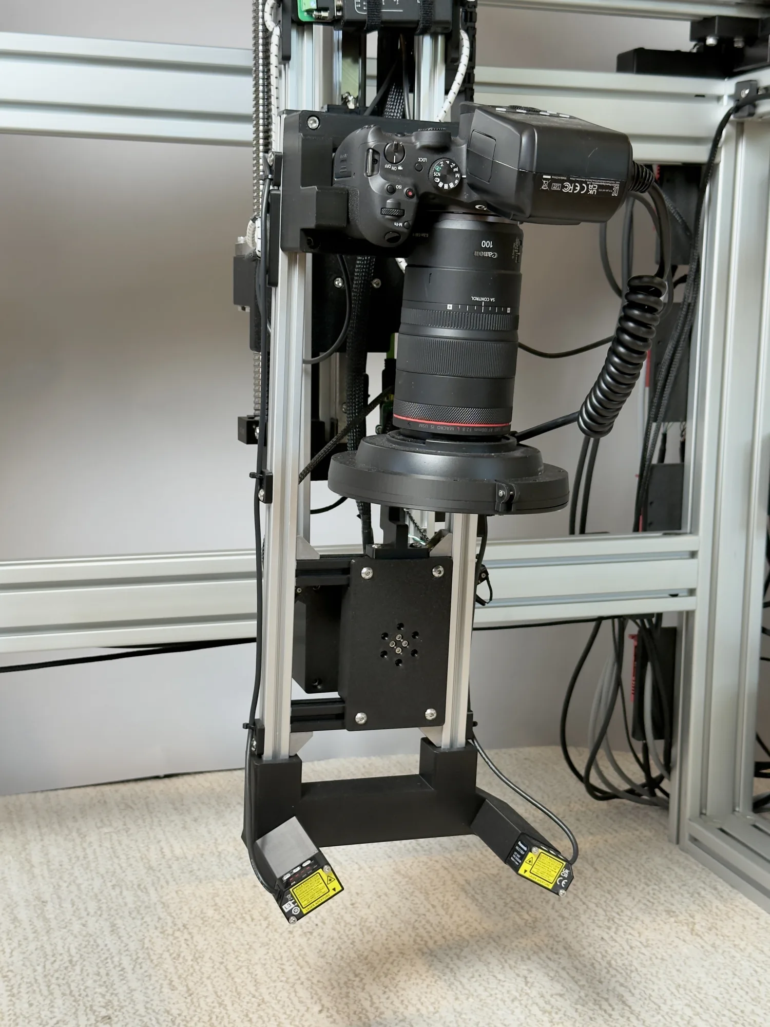 Close-up of the OpenDerm sensor head: a Canon EOS R7 body, a Canon RF 100mm macro lens, a Godox MF-R76 flash with cross-polarization filter, and two downward-facing laser distance sensors.